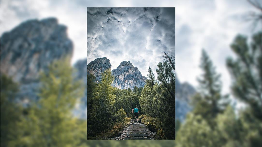 Trailrunner beim schweißtreibenden  Aufstieg über hölzerne Treppenstufen und  alpine Pfade vor einer massiven Felswand in den Dolomiten